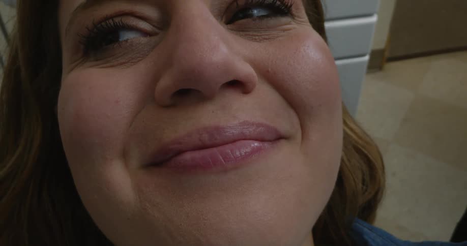 A woman holds her mouth open while a dentist inspects her teeth with a mirror