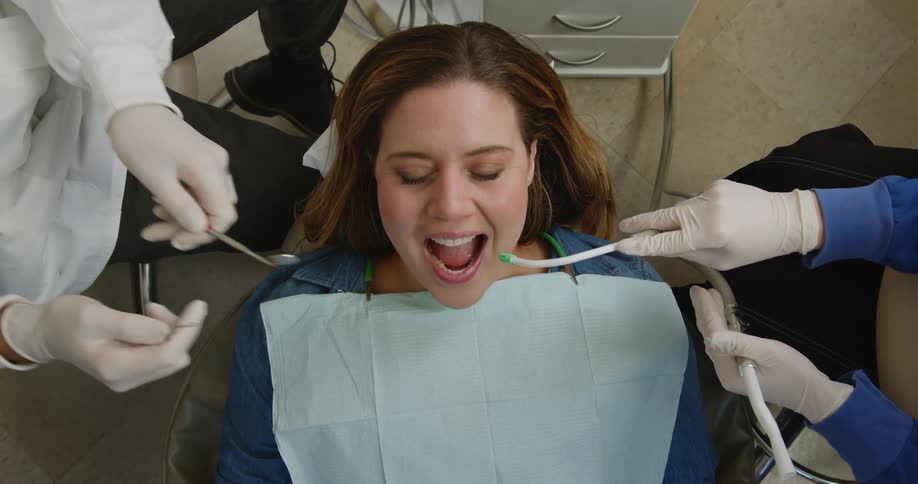 Seated dentist treats female patient using mouth mirror and explorer at dentist clinic