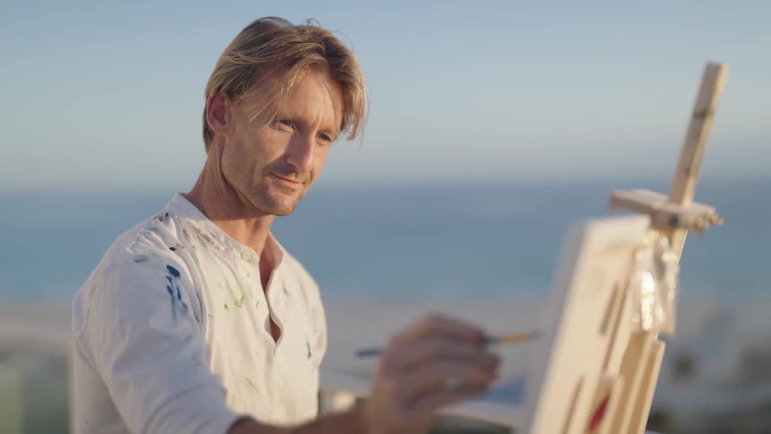 A man is outdoors and is painting on a canvas