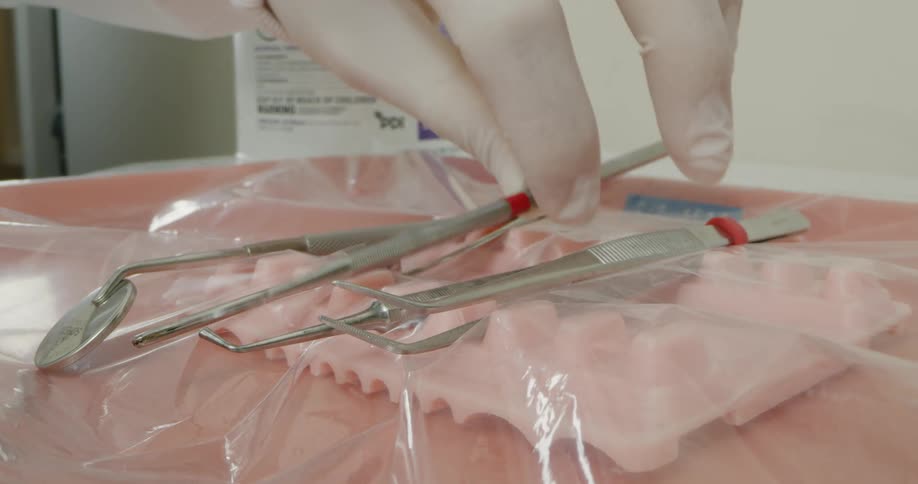A gloved hand places an additional dental tool on a plastic sheet