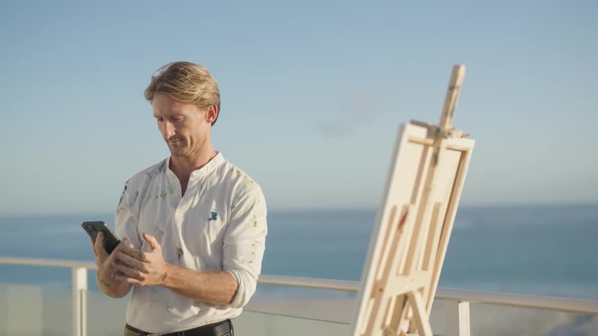 A man hangs up his phone and begins painting