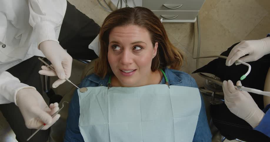 A woman listens to a dentist and their assistant during her examination