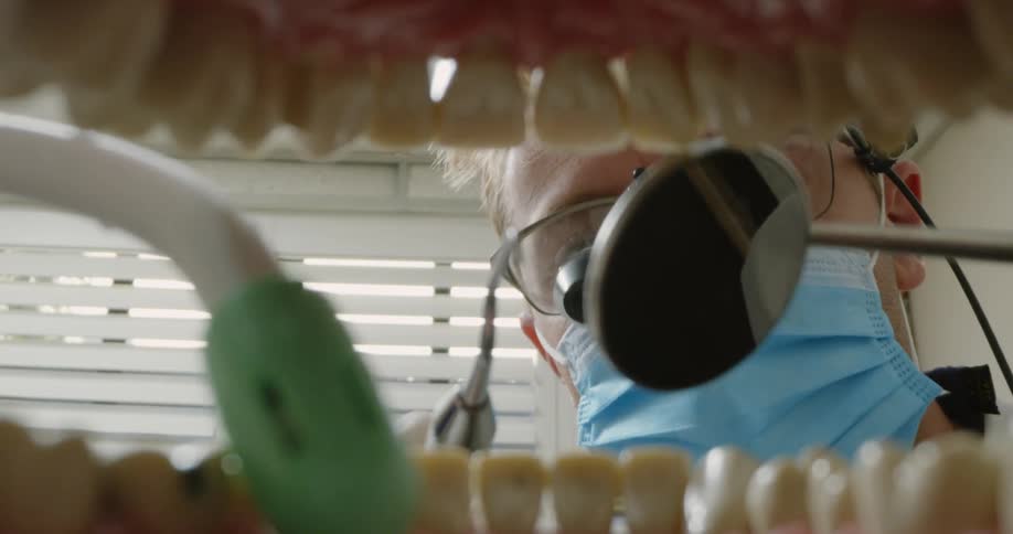 A dentist holds up a mirror as he shines a flashlight into a patients mouth