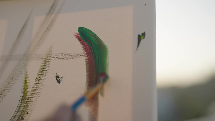 A man paints colorful lines on canvas while painting outside