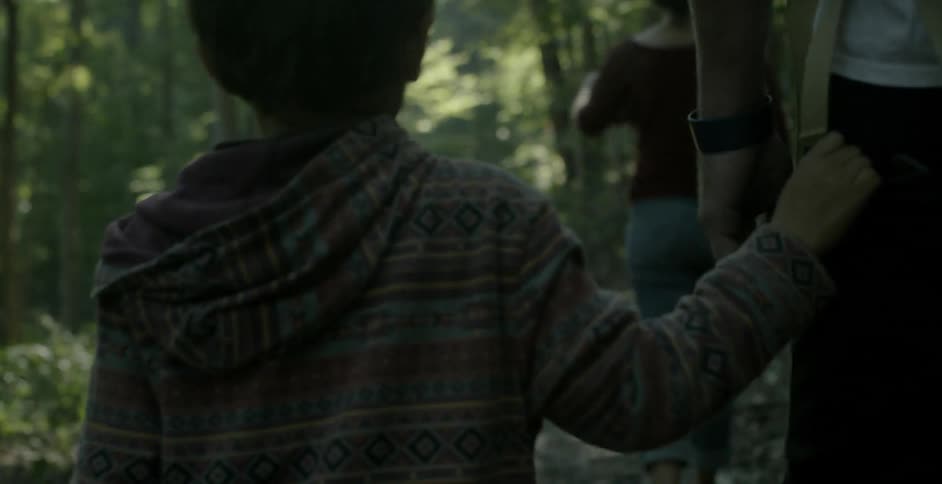 A child holds on to the pocket of their parent while walking through the forest in the day