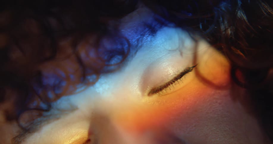 A woman with incredibly curly hair has her eyes closed as the camera rotates in front of her face