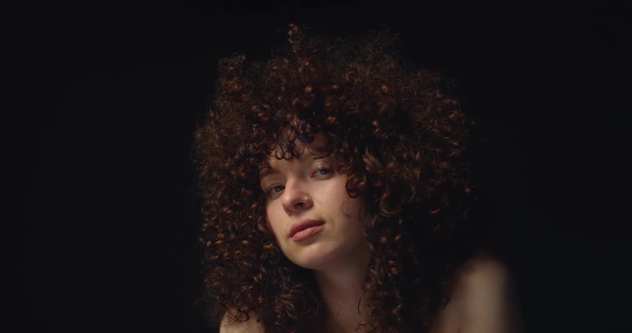 A woman with incredibly curly hair poses and smiles subtly for the camera