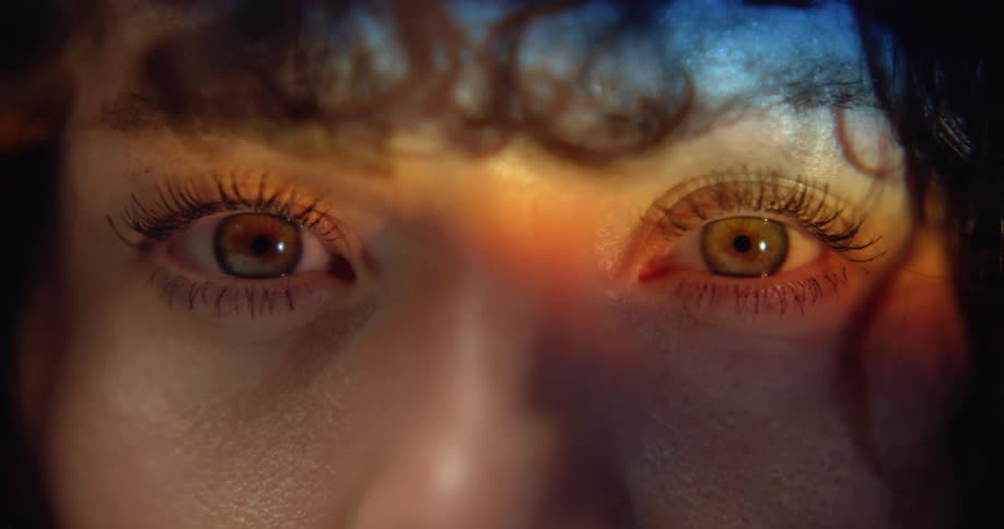 A woman with curly hair opens her eyes and stares directly at the camera