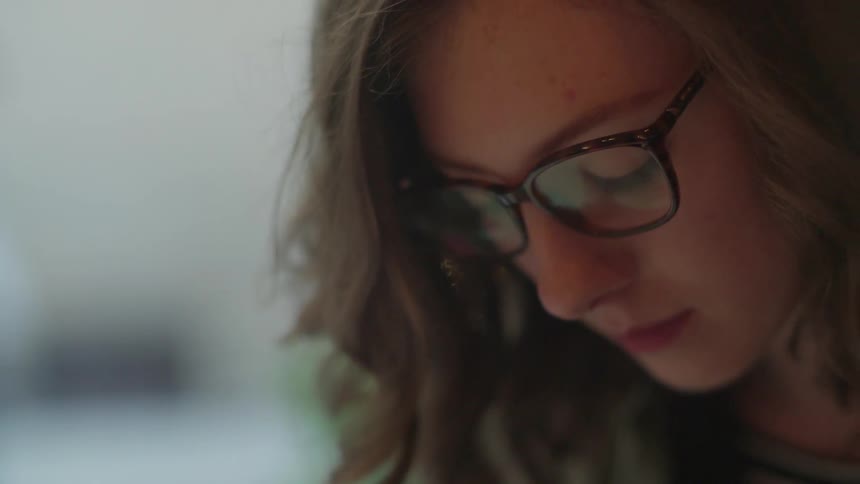 A woman wearing glasses is looking at something below her
