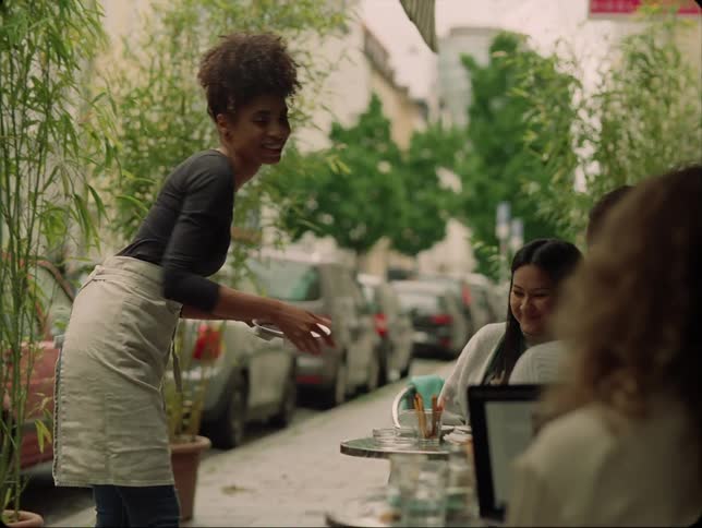 A waitress serves a woman a coffee at an outside cafe