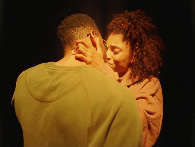 Man wearing glasses and green sweater makes out with woman with curly hair and pink sweater