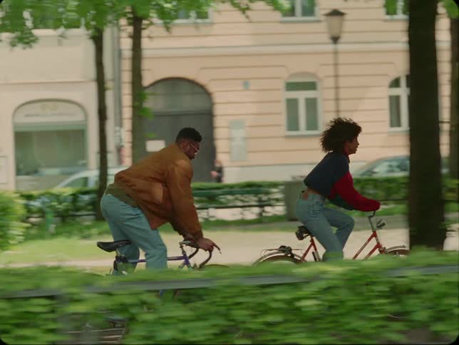 Man and woman ride bicycles along path with building in background