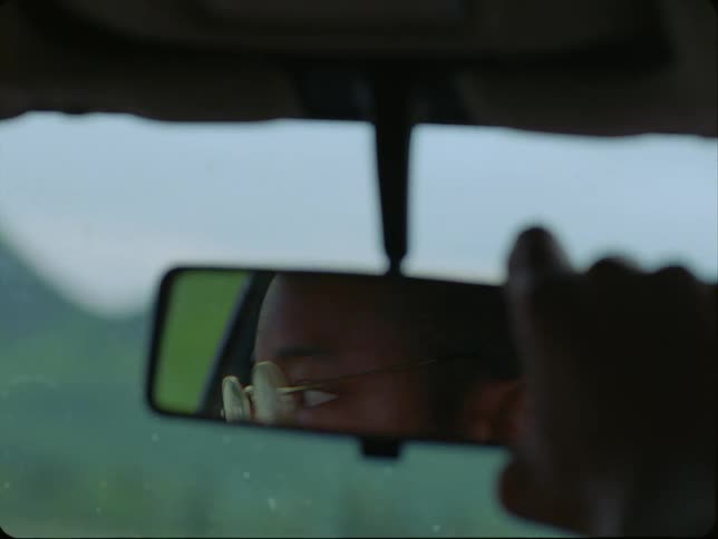 A man looks in the rear view mirror in his car as he adjusts it