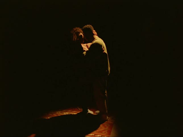 A man and woman are standing together in the darkness with their arms around each other and they kiss