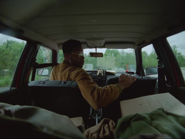 A man looks out the rear window while backing a vehicle out of a parking space in a parking lot