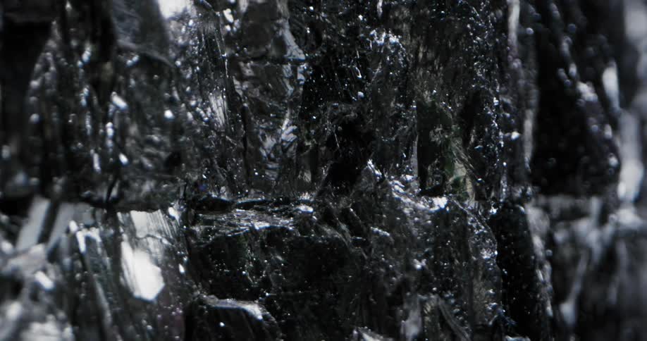 A light reflects off the textured surface of a black gemstone