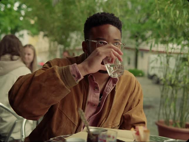 A black male sitting outside writing and drinking at at a table