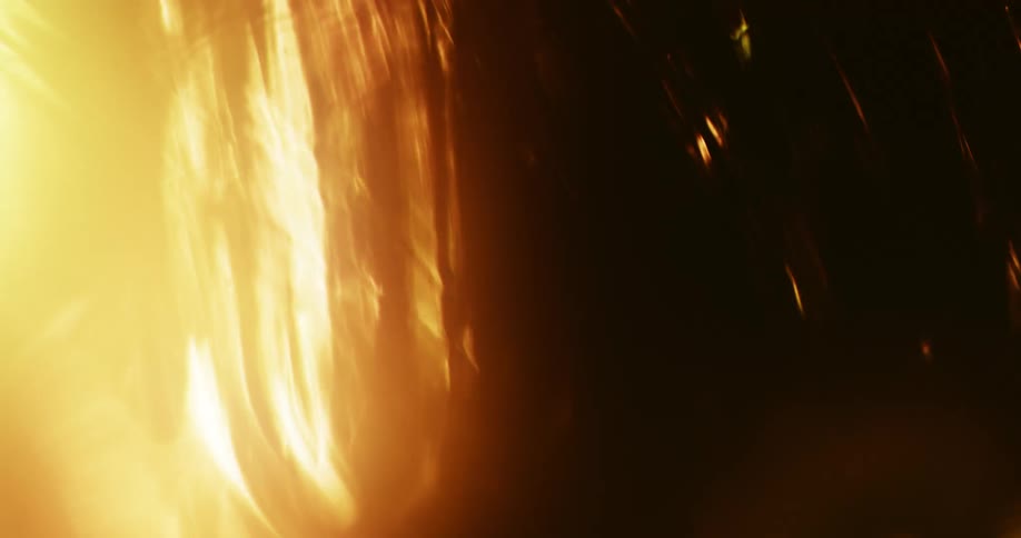A dark organic substance waves and moves as a golden light shines brightly from behind and illuminates the movement