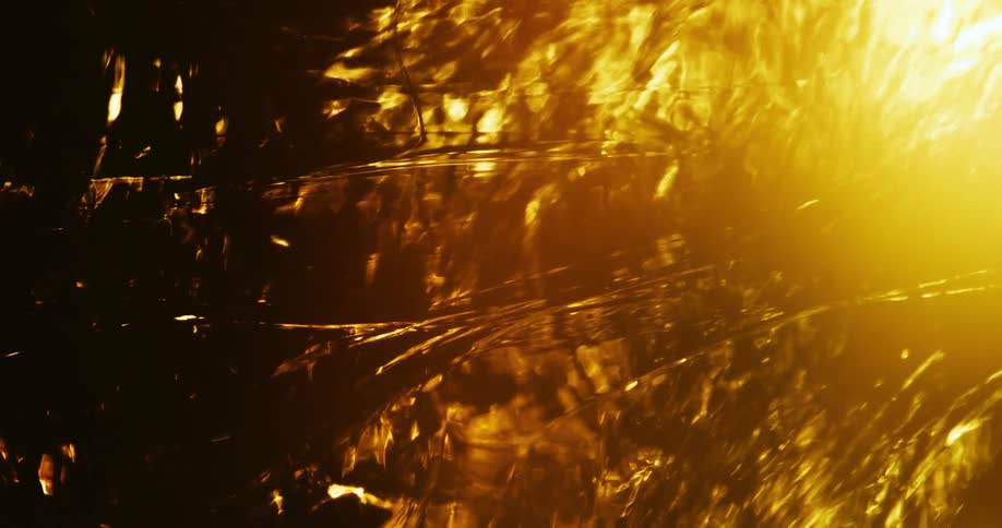 Light shines on amber fluid bringing out highlights and shadows as syrup flows and rotates
