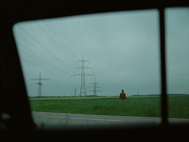 Car window sits parked across road from transmission towers and man