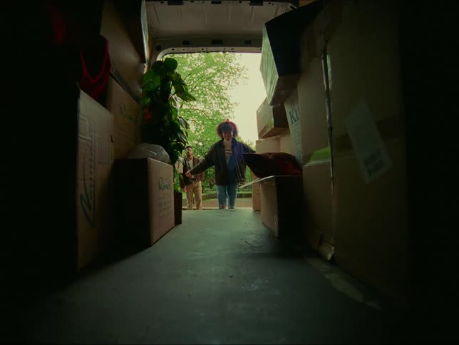 Man watches while girl opens doors and jumps into the back of a moving truck filled with boxes