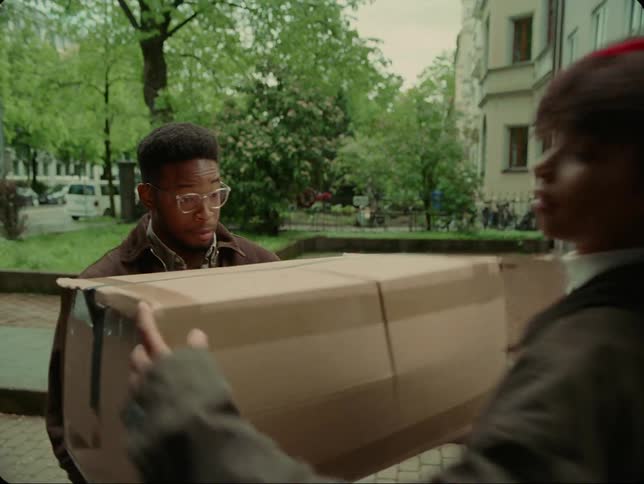 Woman jumps out of moving van parked near apartments with box that she hands to man