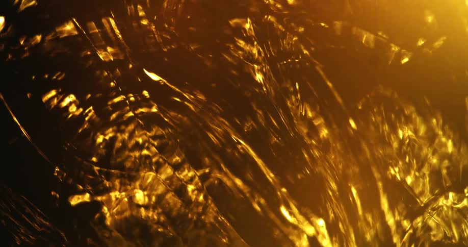 Light shines on amber fluid bringing out highlights and shadows as syrup flows and rotates