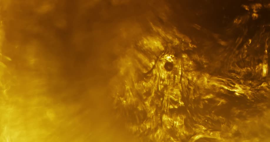 An organic golden substance is moving in the haze as the light creates shadows of the texture as it shines and bubbles rise