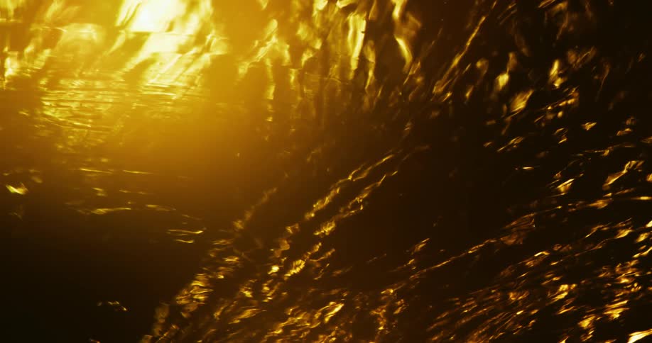 A fluid ripples and swirls as its illuminated by a bright orange light