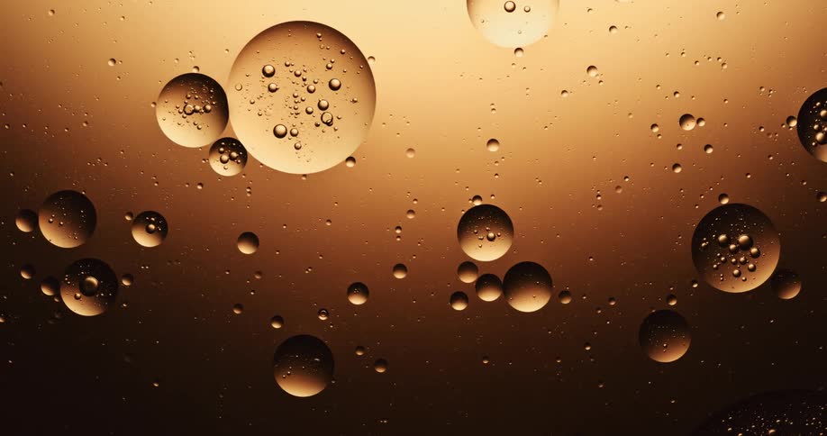 Many spheres with small bubbles inside of them are floating and moving in a golden substance