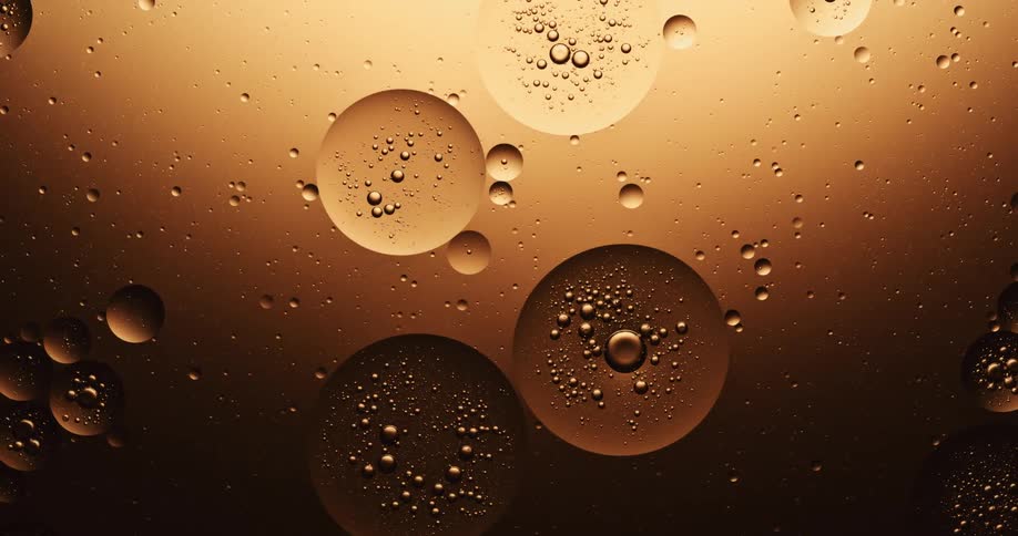 Many spheres are floating in a golden substance with bubbles inside of them and one of them splits into two
