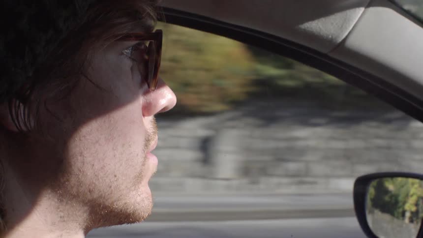 A man wearing glasses drives a car in the day