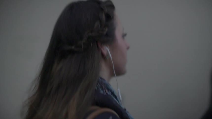 A woman wearing earbuds walks down the road