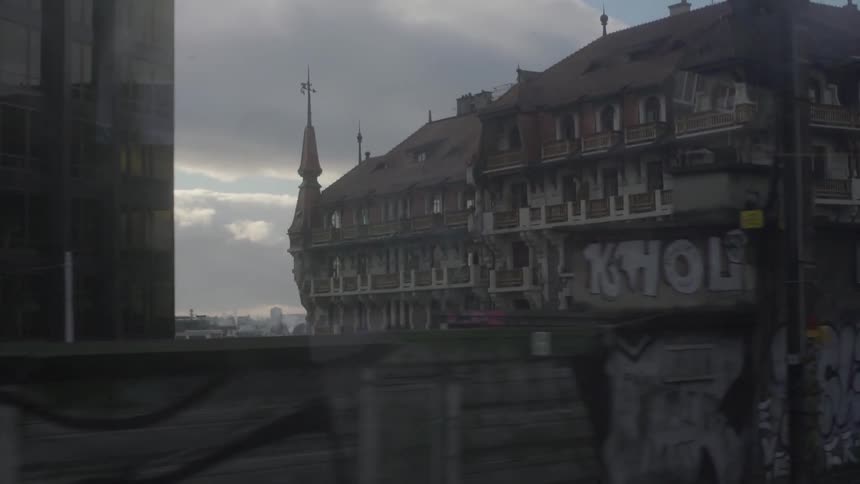 A street barrier covered in graffiti leads to a city building