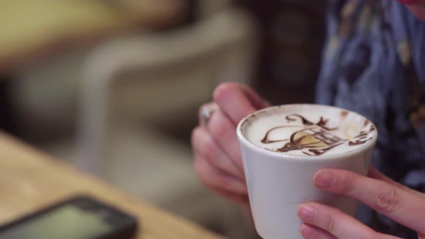 A person takes a drink of a decorated coffee