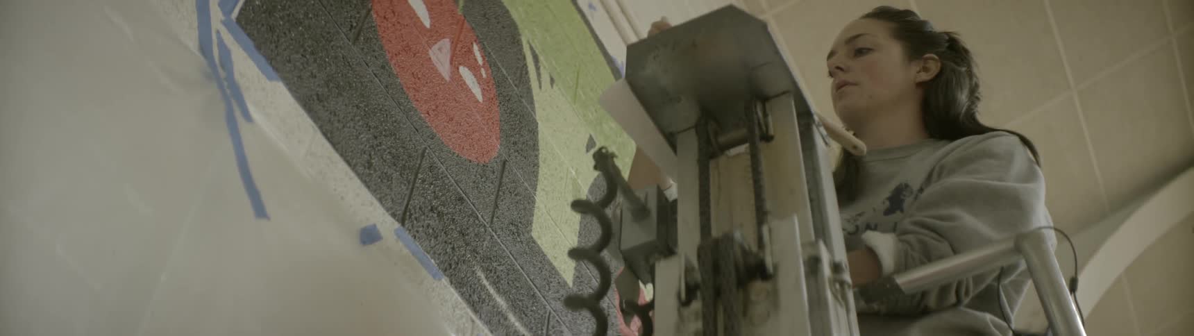 A woman paints a mural on a brick wall