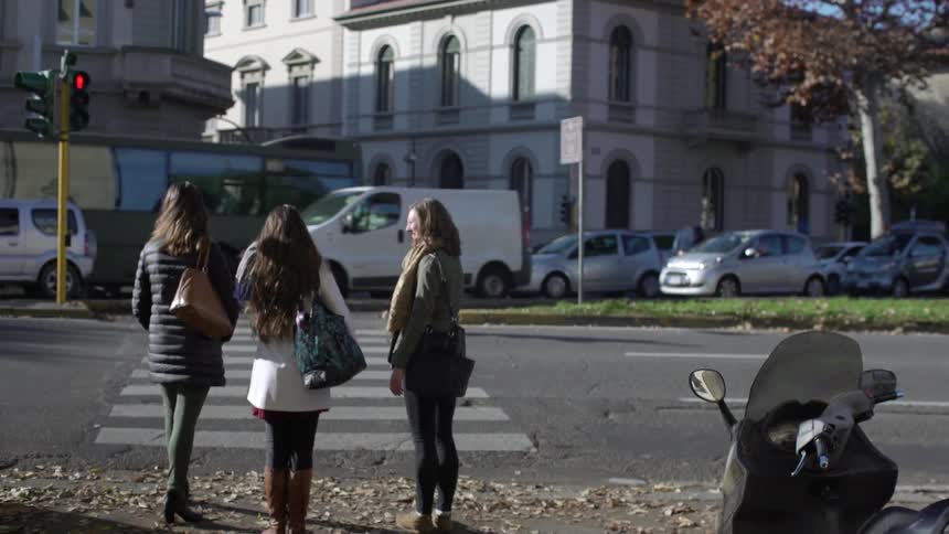 Three women stand at a crosswalk and wait for their chance to go