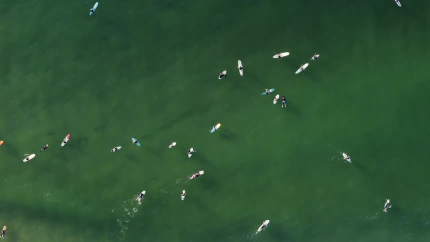 A large number of surfers wait atop their surfboards for waves to form on the ocean