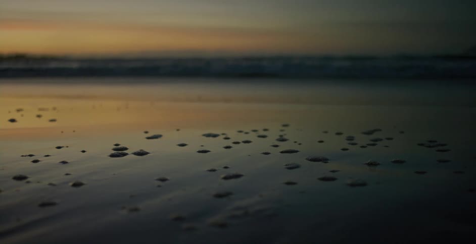 Waves crash high into the shore and leave foam on the sand