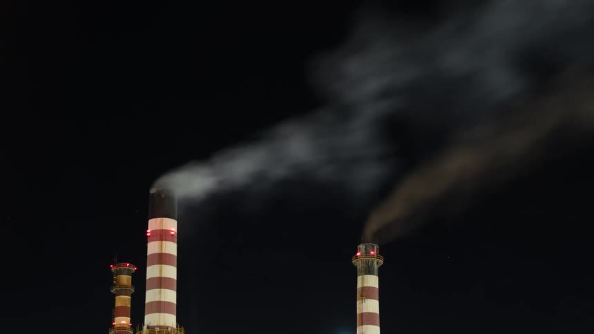 Smoke billows from red and white striped smokestacks at night