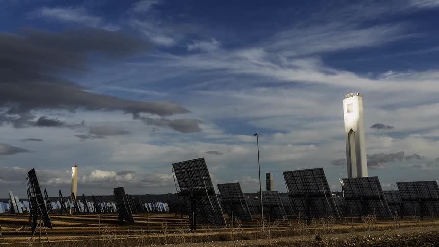 Clouds move rapidly over tower surrounded by solar panels sitting near coast at dusk
