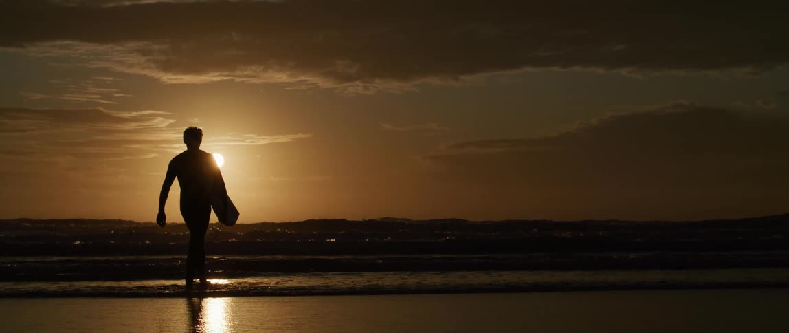 A young white person is walking on the beach and holding there surf board