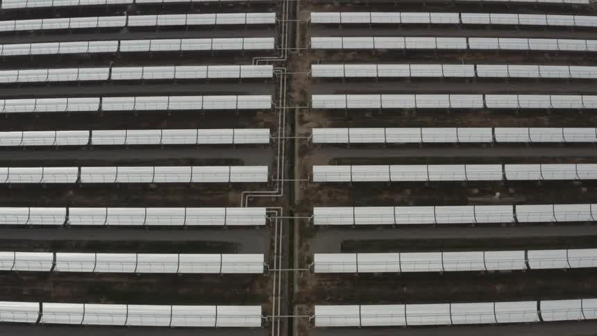Solar panels sit in endless neat repeated rows on the ground
