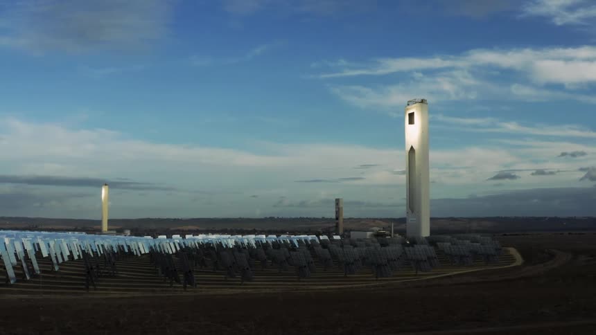 An ominous looking solar collector tower looms over rows of solar panels on a solar farm