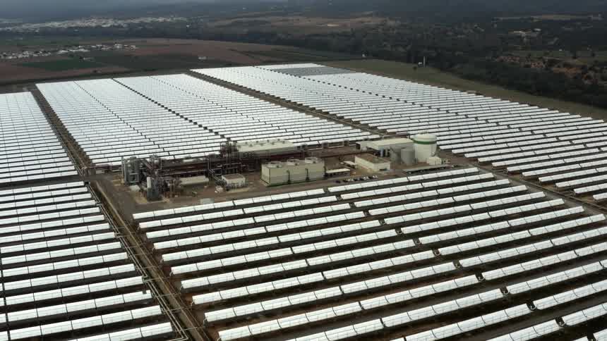 A power plant surrounded by rows of solar panels on a solar farm in a rural area during the day