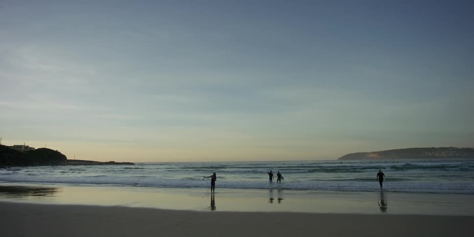 Group of surfers walking into the ocean at dusk