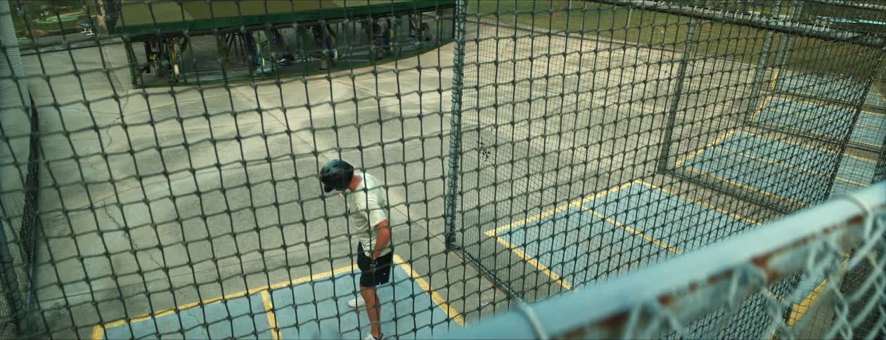 Male batter enters batting cage and waits to swing
