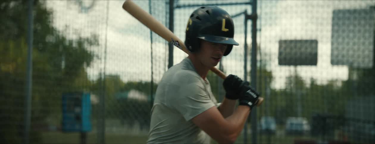 Male batter wears helmet while swinging baseball bat