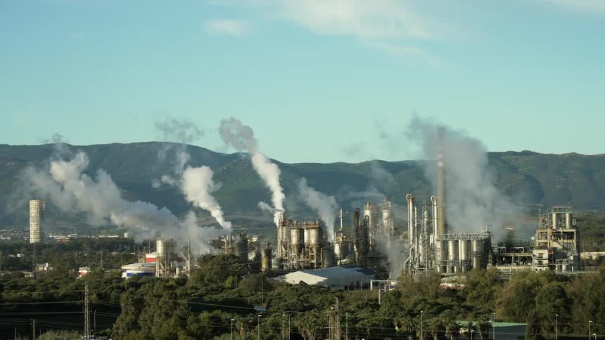 White smoke billows from chimneys at a refinery