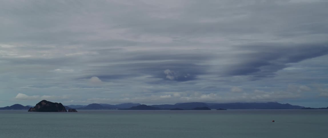 Group of small islands in the calm ocean next to a mountain range in the horizon
